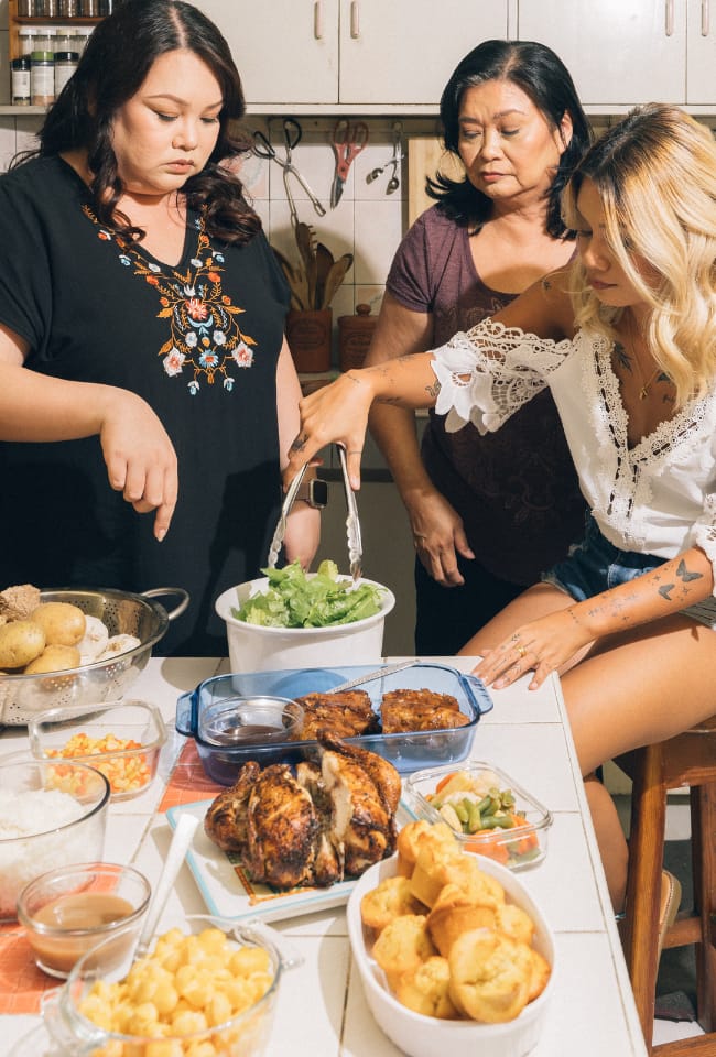 3 women preparing to eat a meal standing at a table.