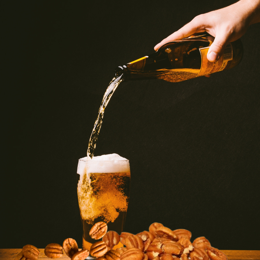 beer pouring from bottle into glass surrounded by pecan halves